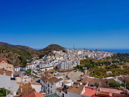 Weiß getünchte Häuser schmiegen sich an einen Hügel in Frigiliana, Spanien. Der Blick reicht über die Dächer bis zum blauen Meer.
