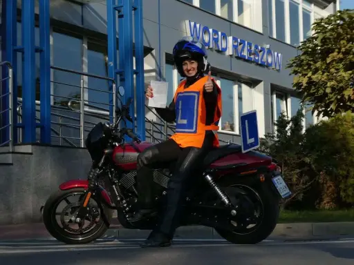 Uśmiechnięta motocyklistka z dokumentem w ręku i kciukiem w górze, gotowa na egzamin teoretyczny kat A.
