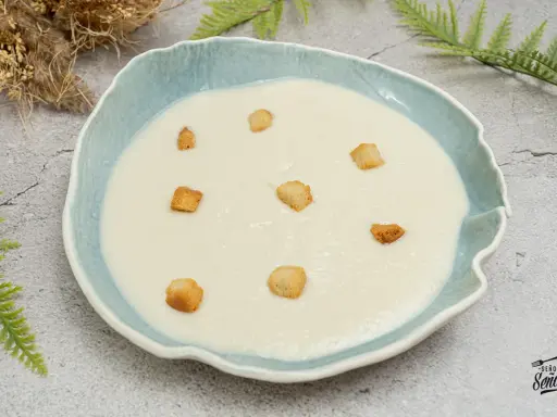 Crema de coliflor suave y cremosa, decorada con crujientes picatostes dorados en un cuenco azul.