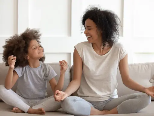 Madre e hija meditando juntas, fomentando sus habilidades de afrontamiento. Ambas sonríen y parecen relajadas.