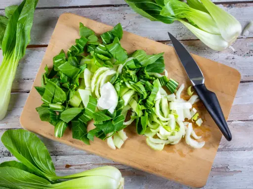 Frischer Pak Choi wird auf einem Holzbrett zerteilt, bereit zum Zubereiten. Ein Messer liegt daneben.