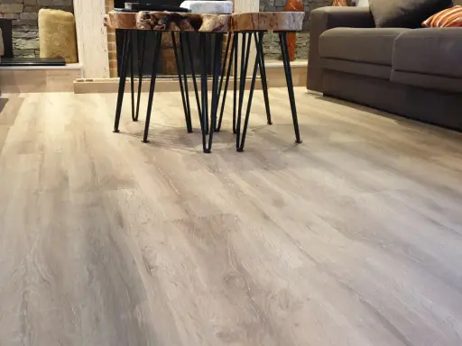 El suelo laminado o parquet de madera clara se extiende por la sala, reflejando la luz.