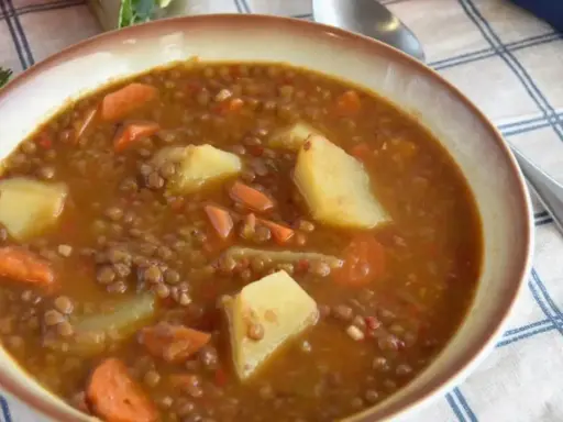 Un plato humeante de lentejas estofadas al estilo Arguiñano, con patatas y zanahorias, listo para disfrutar.
