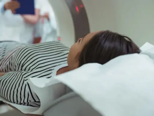 Kobieta leży na stole do rezonansu magnetycznego. Czy na rezonans magnetyczny można mieć hybrydy? Lekarz w białym fartuchu obserwuje badanie.