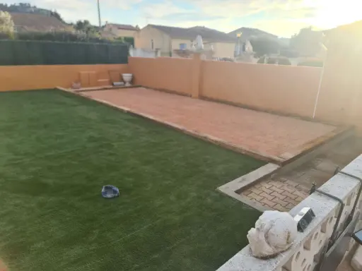 Un terrain de pétanque prêt pour l'entretien, avec une allée en gravier et une pelouse artificielle.