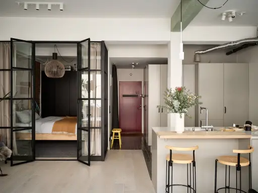 Une chambre en second jour, séparée par des portes vitrées. Une cuisine moderne avec un îlot et des tabourets complète l'espace.