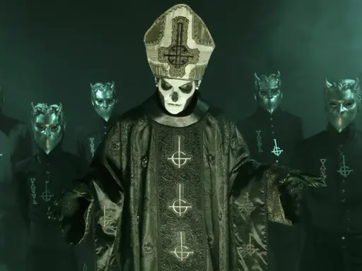 Papa Emeritus IV, klädd i en detaljerad mörkgrön prästrock med korsmotiv, står framför en grupp maskerade följeslagare med horn.