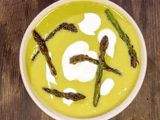 Crema di asparagi vellutata, guarnita con asparagi croccanti e un tocco di panna.