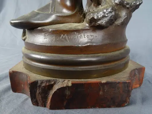 Signature "Eug. Marioton" gravée sur la base d'une sculpture en bronze patiné, posée sur un socle en marbre rouge.