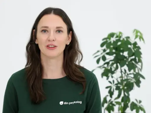 En kvinna med mörkt hår och blå ögon, klädd i en grön tröja med texten "din psykolog", talar. Bredvid henne står en grön växt. Hon ger dig verktyg att hantera sorg.