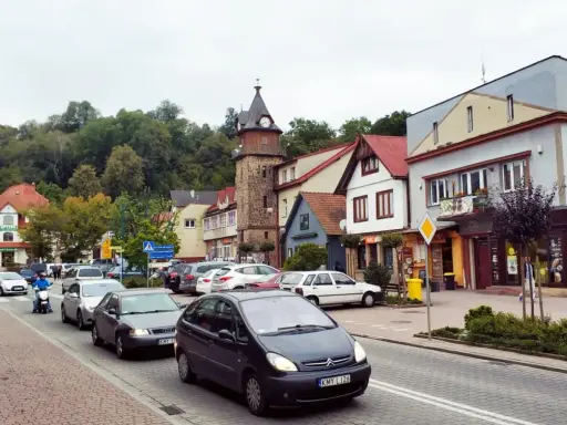 Tłoczny dobczyce rynek z wieżą zegarową, samochodami i skuterem.