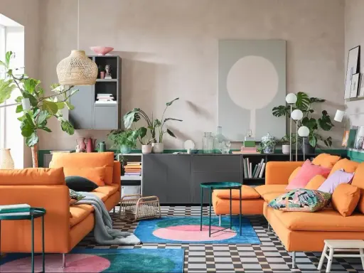 Un salon moderne avec deux canapés orange vif. Un tapis rond aux couleurs vives et des plantes vertes apportent de la vie. L'idée est d'associer 2 canapés différents pour un style unique.