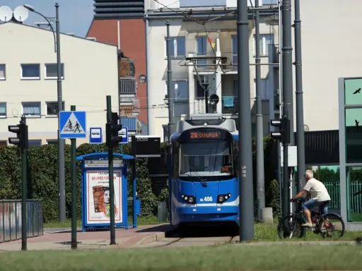 Niebieski tramwaj na przystanku w Krakowie, obok rowerzysta i znaki drogowe.