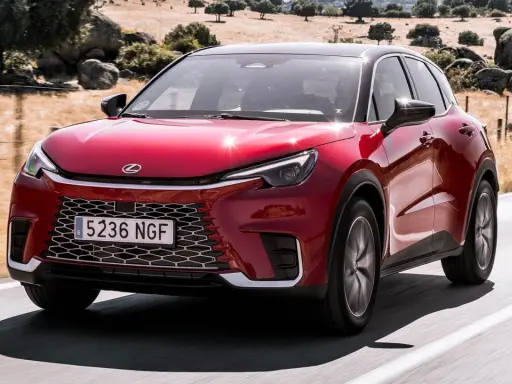 El Lexus LBX rojo brillante se desplaza por una carretera rural, con un paisaje seco y rocoso de fondo.
