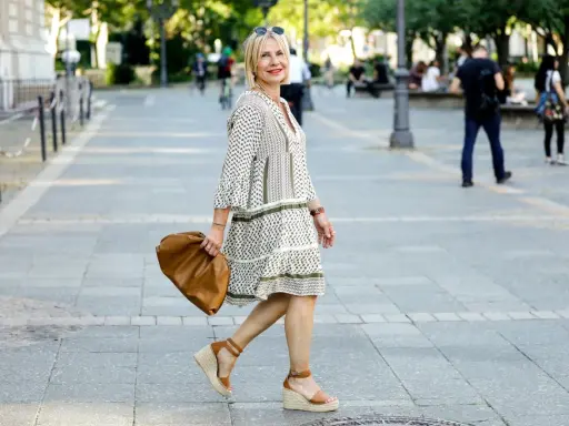 Kobieta w sukience w geometryczne wzory i espadrylach na koturnie idzie ulicą z brązową torebką.