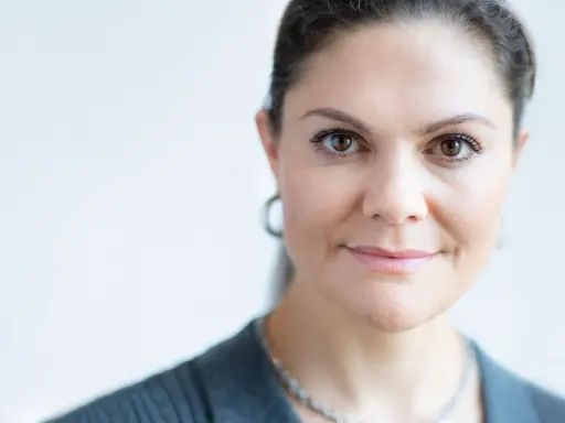 Kronprinsessan Victoria ålder. En närbild av hennes ansikte med bruna ögon och ett leende. Hon bär en grå kavaj och ett silverhalsband.