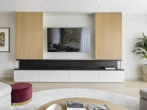 Un moderno mueble de salón con una gran televisión para poner la tele en medio del salón. Destacan los paneles de madera clara y los cajones blancos.
