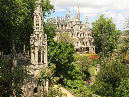 Sintra co zobaczyć: Quinta da Regaleira z wieżą i pałacem, otoczona bujną zielenią i kolorowymi rabatami.