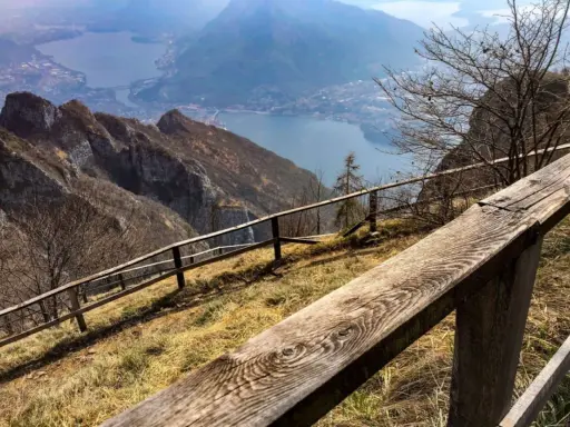 Sentiero con staccionata in legno per una passeggiata sul Pian dei Resinelli, con vista panoramica sul lago e le montagne.
