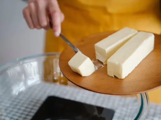 Ein Stück Butter wird mit einem Messer von einem Holzbrett gehoben, bereit für die Zubereitung von Butterschmalz.