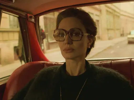 Angelina Jolie i en bil, en scen från en av hennes filmer. Hon bär stora glasögon och tittar ut genom fönstret.