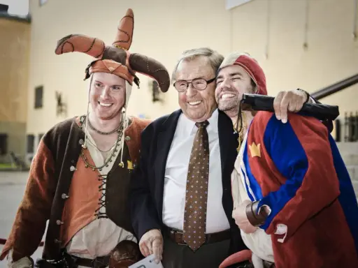Jonas Elgh skrattar med två män i medeltida kläder. En har en narrmössa, den andra en röd och blå dräkt.
