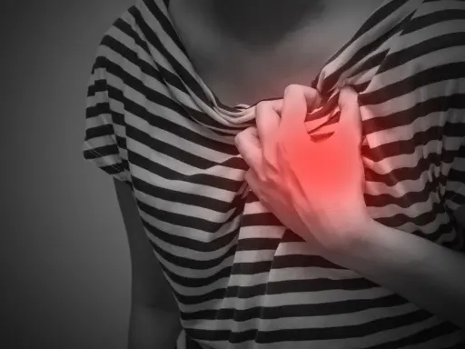 Brustschmerz, ein mögliches Symptom von zu viel Koffein. Eine Hand greift schmerzhaft zur Brust.