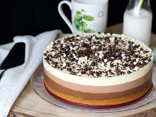 Deliciosa tarta de tres chocolates, con capas de blanco, con leche y negro, cubierta de virutas y bolitas de chocolate.