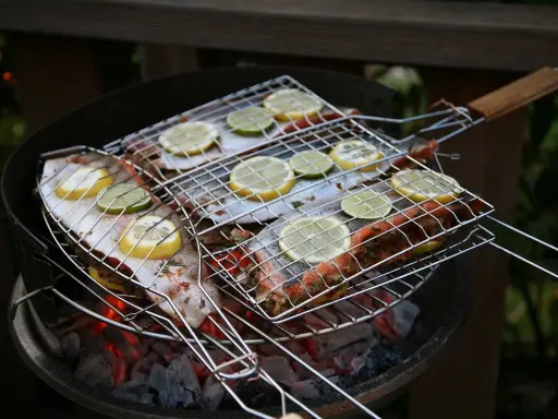 Grillad fisk med citron- och limeklyftor på en kolgrill. Doften av sommar och god mat sprider sig.