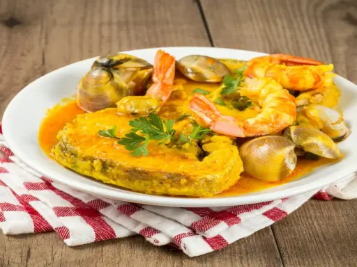 Plato de comida asturiana con un trozo de pescado, gambas y almejas en salsa.