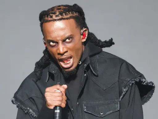 Playboi Carti z mikrofonem, w czarnej kurtce i z charakterystycznymi warkoczami. Jego ekspresja sugeruje energię znaną z jego playboi carti utworów.