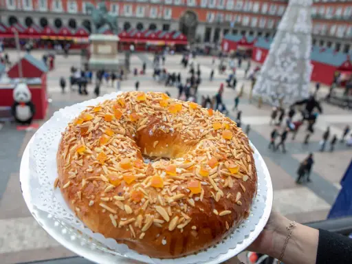 El mejor roscón de Madrid, adornado con almendras y fruta confitada, se presenta en la Plaza Mayor, un festín visual y delicioso.