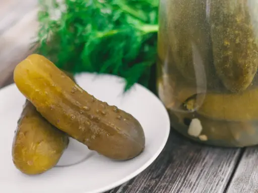 Dwa ogórki kiszone na talerzyku, obok słoik pełen kiszonków. Zastanawiasz się, dlaczego ogórki kiszone są puste w środku? To proces fermentacji!