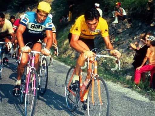Eddy Merckx heute im Gelben Trikot, kämpft sich einen Berg hinauf. Fans jubeln am Straßenrand.