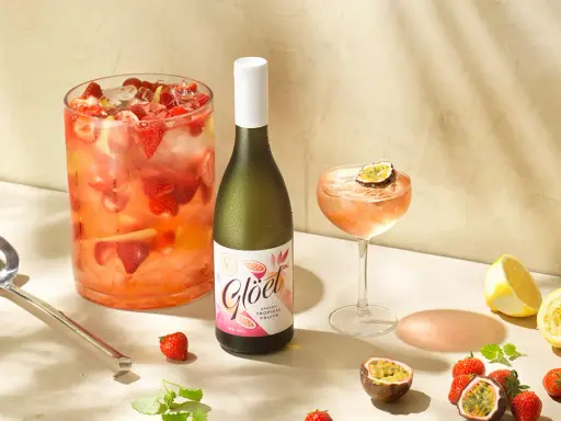 En stor bålskål fylld med jordgubbar och is, en flaska vitt vin och en cocktail med passionsfrukt. Perfekt för en somrig drink med vitt vin.