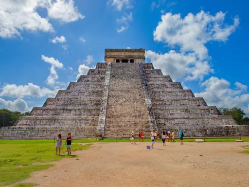 Majestatyczna piramida w Chichen Itza, z turystami podziwiającymi jej piękno na tle błękitnego nieba.