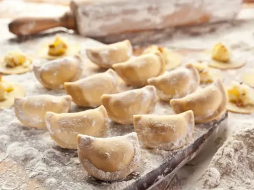 Gotujesz pierogi? Zobacz, jaka mąka do pierogów będzie najlepsza! Na zdjęciu świeżo lepione pierogi, wałek i rozsypana mąka.