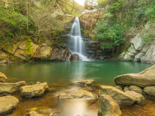 Cascada en un entorno verde con aguas cristalinas, evocando la belleza de las piscinas naturales de Cádiz.
