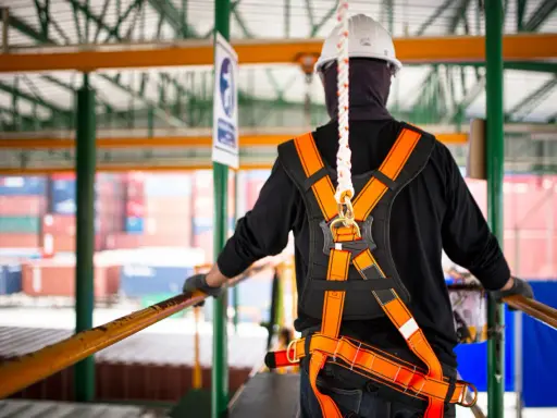 Trabajador con arnés de seguridad naranja y blanco, listo para trabajar en altura. La vida útil de un arnés de seguridad depende de su uso y mantenimiento.