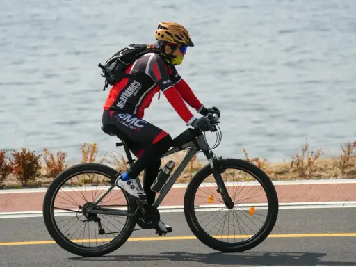 Rowerzysta w kasku i masce jedzie rowerem wzdłuż jeziora. Idealne noclegi dla rowerzystów czekają po wyczerpującej trasie.
