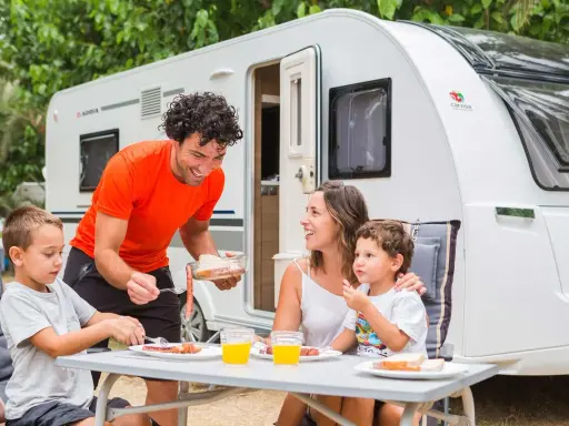 Familia disfrutando de un picnic en campamentos para familias, con una caravana de fondo.
