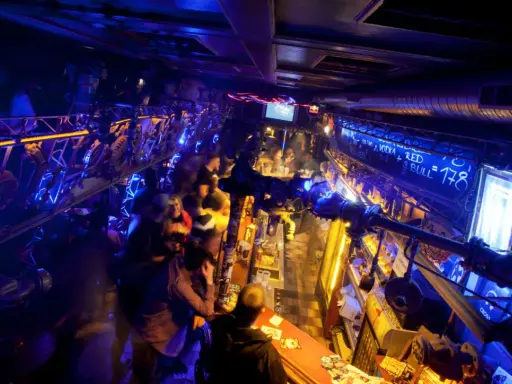Lebhafte Nacht in einem der Prager Clubs, beleuchtet von blauem und gelbem Licht. Menschen stehen an der Bar und unterhalten sich.