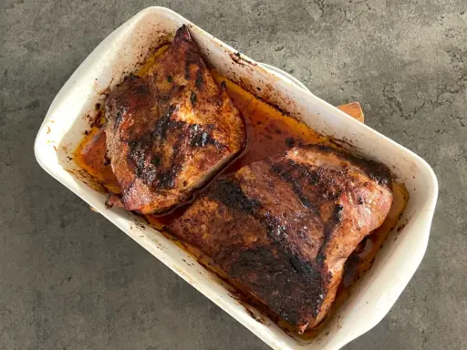 Två saftiga bitar av grillad pluma ligger i en vit ugnsform, redo att serveras.