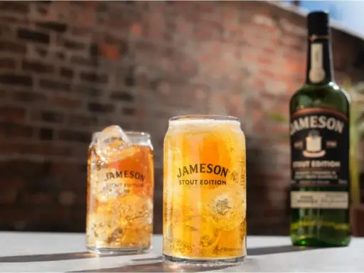 Dwa orzeźwiające drinki z lodem i butelka Jameson Stout Edition na tle ceglanej ściany.