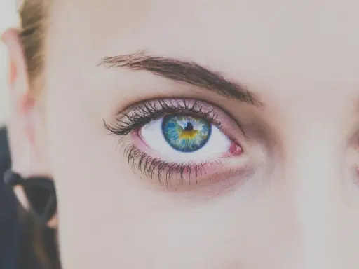 Ojo con iris azul y amarillo, pestañas largas y cejas definidas tras un laminado de cejas.