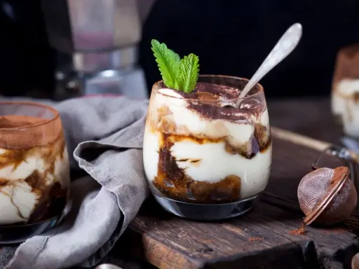 Pyszne tiramisu w pucharkach, udekorowane listkiem mięty, na drewnianej desce.