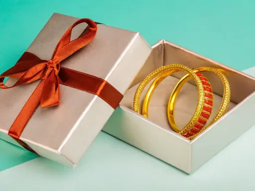 Scatola regalo aperta con bracciali dorati e rossi. Come capire se un bracciale è oro? Osserva la lucentezza e i dettagli.