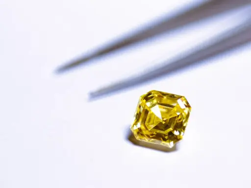 Un brillante giallo intenso, simile a un tesoro di **oro 18 carati**, attende di essere incastonato. Pinzette sfocate sullo sfondo.