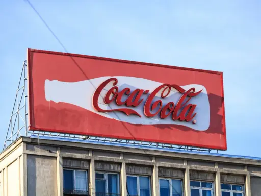 Duży baner logo Coca-Cola na dachu budynku, z charakterystyczną białą butelką i czerwonym napisem.