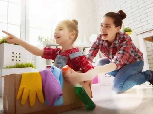 Mama i dziecko bawią się w sprzątanie, ucząc się jak nauczyć dziecko sprzątać. W kartonie są rękawice i płyn.